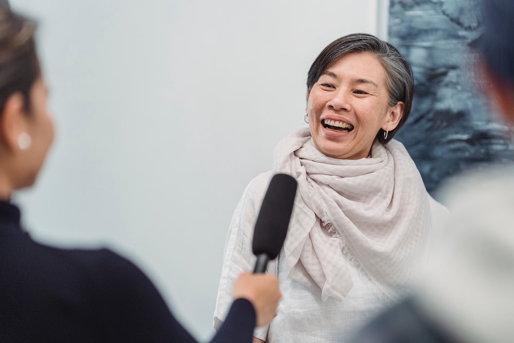 A smiling woman speaking with a reporter.