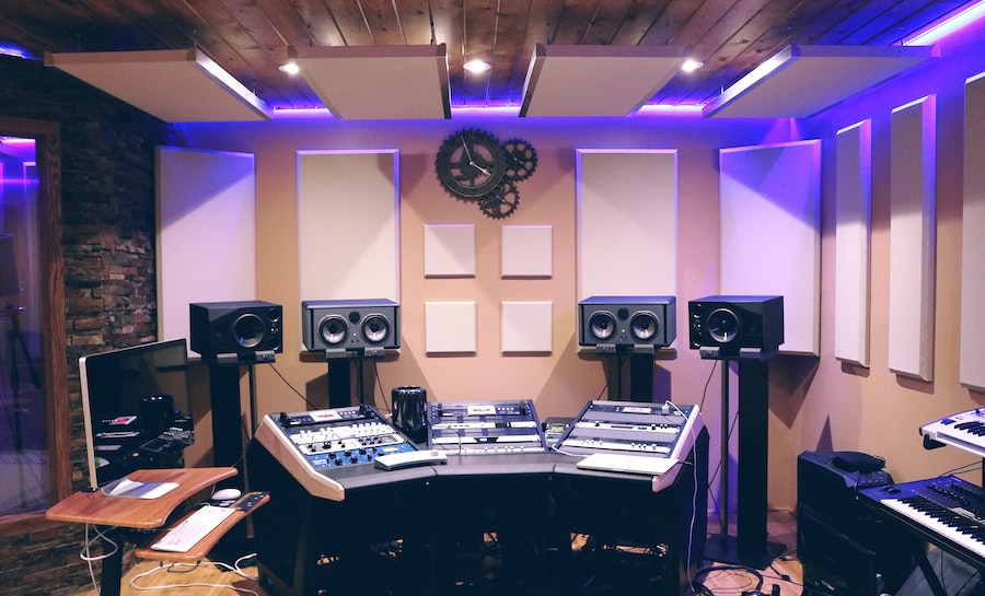 A padded room with an audio mixing table and four large standing speakers