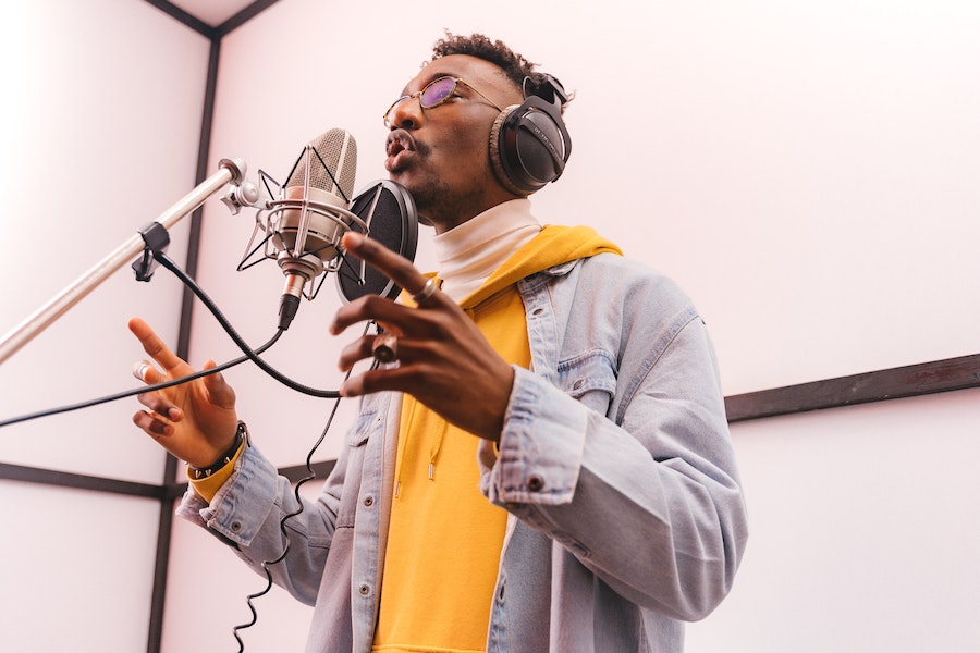 A man wearing headphones while singing into a standing microphone.