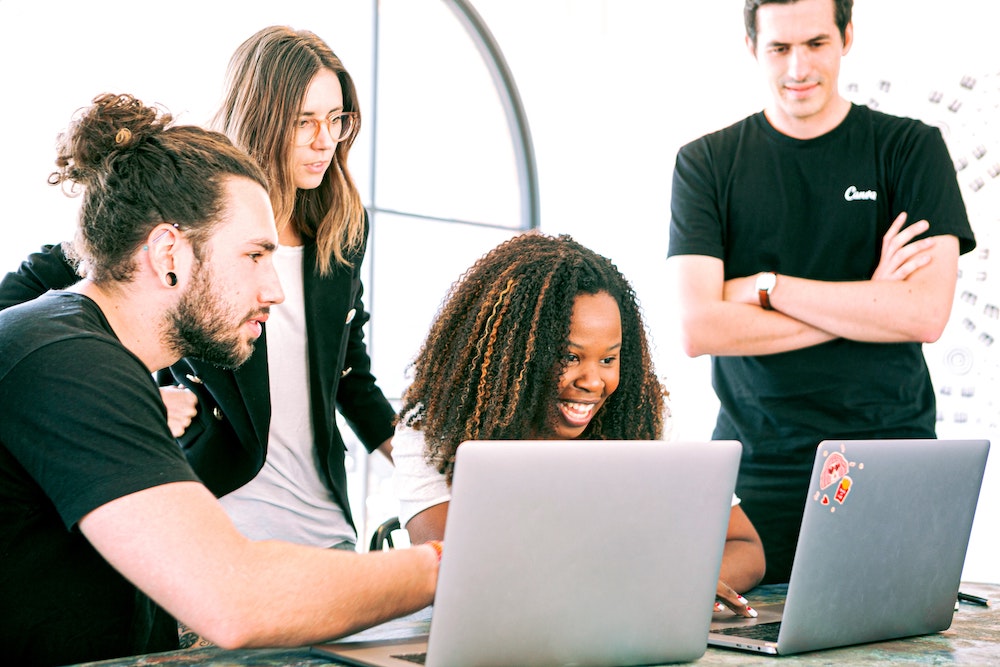 Four people collaborating around two laptops.